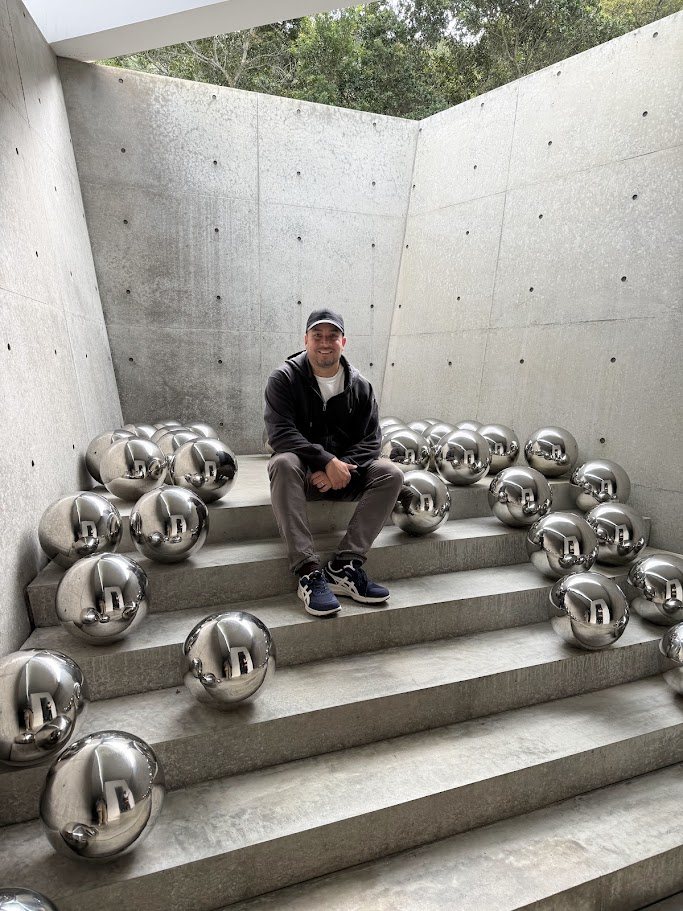 Rodrigo sentado en una escalera de hormigón, rodeado de esferas de acero inoxidable, en Naoshima, Japón.